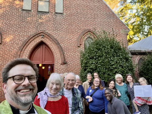 Group of diverse people smiling outside All Hallows Parish church.