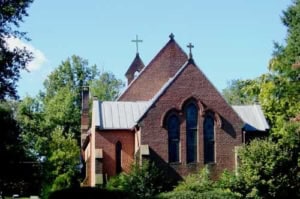 All Hallows Parish church with brick architecture and steeples in a lush setting.